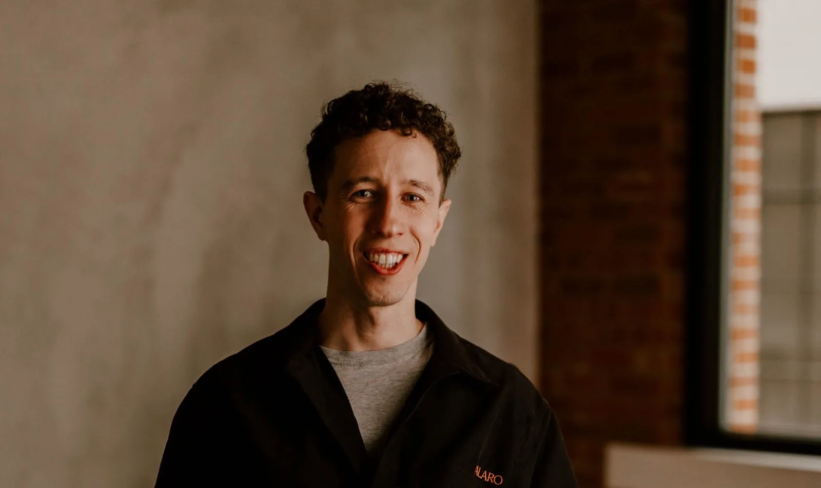 Francisco Moretti, creator of ChatJS, smiling in a sunlit room with a concrete wall and a brick-framed window behind him