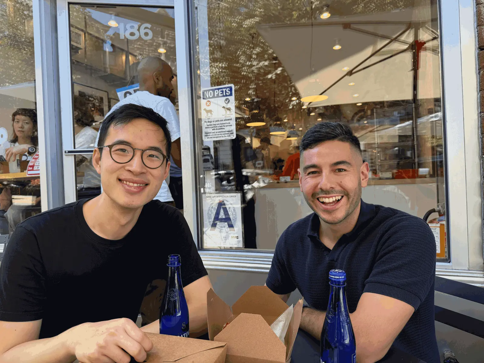 Francisco, right, and a colleague smiling over lunch at a sidewalk café table